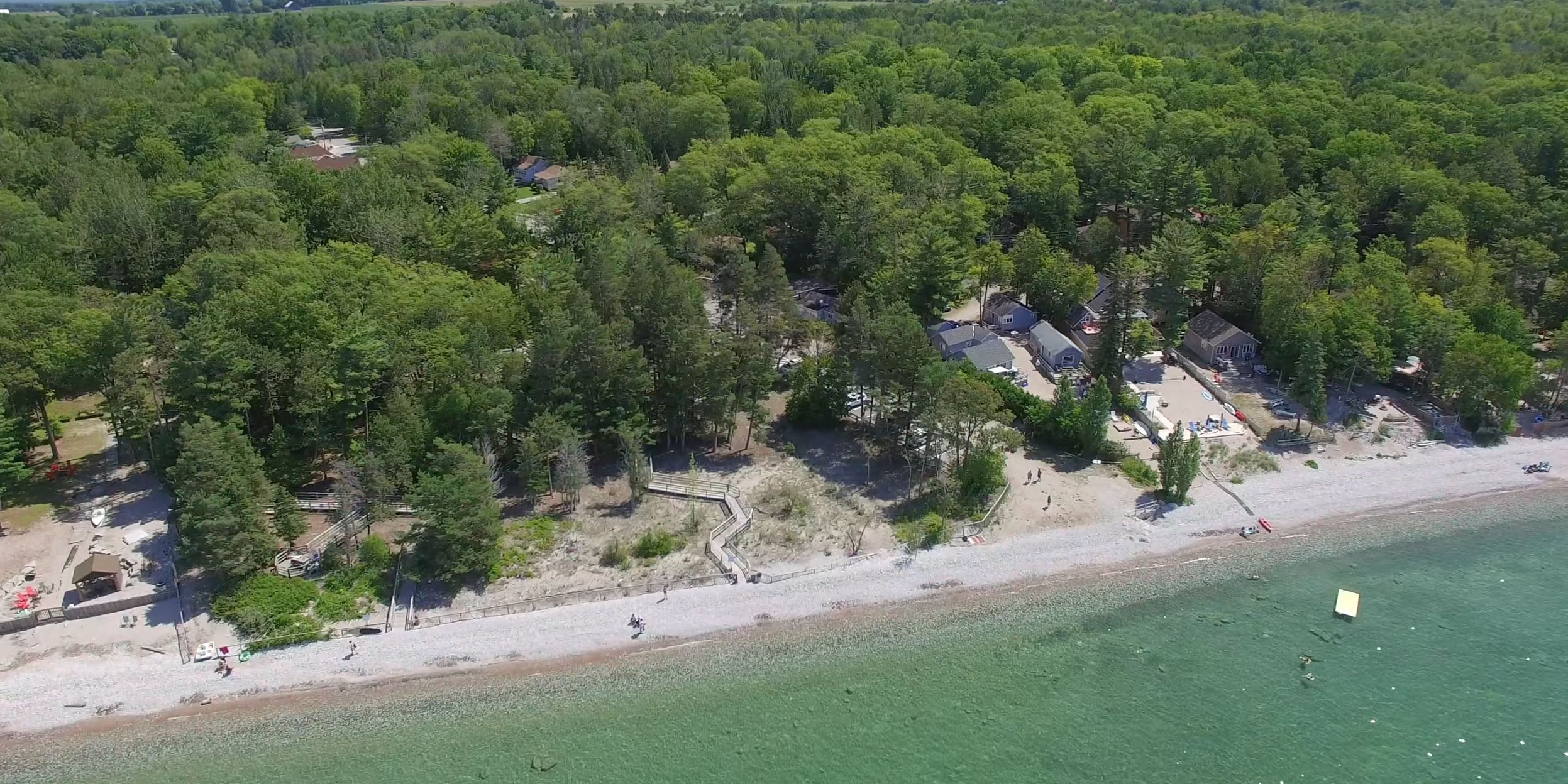 Aerial view of Woodland Beach, surrounded by dense green forests, cottages, and clear turquoise waters